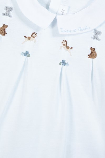 Gaiši zilā krekls ar apkakles izgriezumu, ar izšūtiem dzīvniekiem (suņiem, lāčiem un ziloņu) un dekoratīviem akcentiem.