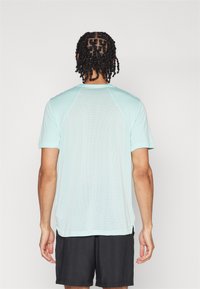 Lyseblå treningst skjorte med teksturert bakside, korte ermer og rund hals, kombinert med svarte shorts.