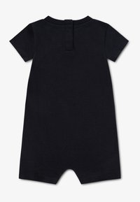 Melns īsroku kombinezons ar apaļu izgriezumu, aizmugurē pogu aizdare un mīksts, teksturēts audums. Nav redzamu rakstu vai akcentu.