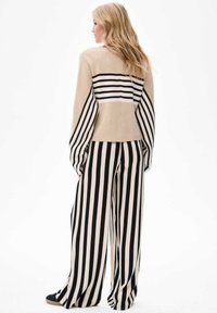 Beige gebreide trui met zwart-witte horizontale strepen, gecombineerd met brede zwarte en witte verticaal gestreepte broek. Gladde textuur.