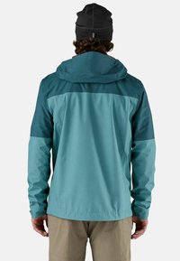 Giacca impermeabile con cappuccio in blu-verde, con un design bicolore, dotata di maniche lunghe e polsini regolabili. Tessuto texture.