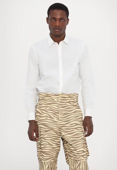 Witte longsleeve shirt met knoopsluiting, gecombineerd met beige cargobroek met een bruin zebra-patroon en cargovakken.