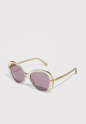 Lunettes de soleil rondes avec monture beige translucide, verres violets et petits accents décoratifs dorés près des charnières.