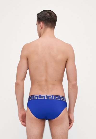 Blaue Badeunterhose aus Stretchstoff, mit einem goldenen griechischen Schlüssel-Muster am Bund. Glatte Textur und taillierte Passform.