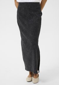 Maxi skirt in dark gray fabric with a textured finish, featuring a side slit for ease of movement. Paired with cream-colored shoes.