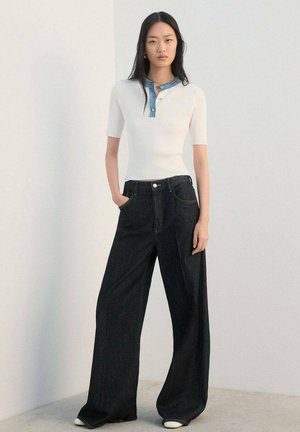 Top blanco de manga corta con textura acanalada y cuello de mezclilla, combinado con pantalones vaqueros anchos de pierna ancha en azul oscuro y de corte holgado. Diseño sencillo, materiales de calidad.