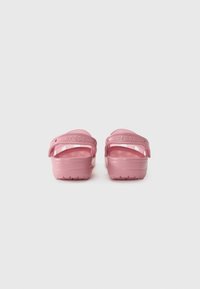 Pink Crocs clogs with a textured surface and two rear straps, featuring the brand name embossed on each strap. Flat, thick soles.