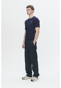 Navy short-sleeve t-shirt with a small red logo on the chest, paired with dark loose-fitting pants and light athletic sneakers.