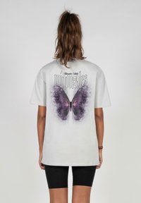 Gray cotton t-shirt with a large purple butterfly graphic on the back, featuring a distressed splatter design and bold typography above.