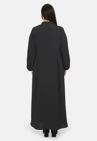 Langes schwarzes Kleid mit strukturiertem Design, rundem Kragen und Ballonärmeln, das einen fließenden Rock und einen subtil strukturierten Stoff besitzt.