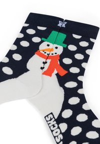 Chaussettes bleu marine à pois blancs avec un design de bonhomme de neige portant un chapeau vert et une écharpe rouge. Matière en mélange de coton, texture douce, longueur cheville.