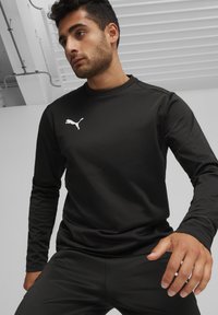 Zwarte sportieve lange mouwen top van glad, lichtgewicht materiaal, met een klein wit Puma-logo op de borst, gecombineerd met bijpassende broek.