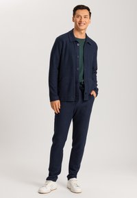 Cárdigan de punto navy con cuello, botones y dos bolsillos frontales, combinado con pantalones navy a juego y zapatillas blancas. Textura suave.