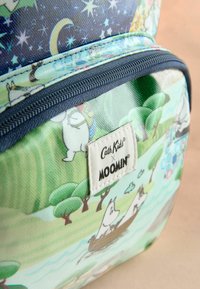 Bērnu mugursoma ar Mūmiju varoņiem, kas laivo pa upi zem zvaigžņu debesīm, pie krasta augot kokiem.