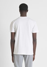 Witte katoenen t-shirt met korte mouwen en een ronde hals, met een eenvoudig ontwerp en een gladde textuur, gedragen met lichtgrijze broek.