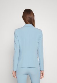 Jasnoniebieska marynarka z gładkiego materiału. Charakteryzuje się dopasowanym krojem, wyłogami z nacięciem, długimi rękawami oraz bocznymi kieszeniami.