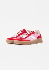 Sneakers in suede rosso e rosa con dettagli bianchi, caratterizzati da una suola in gomma, punta rotonda e lacci piatti. Il design include pannelli di colore a strati.