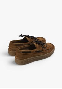 Brune ruskindsko med rund tå, sorte snørebånd og en tekstureret, tyk sål. Har et lavskåret design og subtile sideaccentuer.