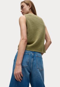 Chunky gebreide mouwloze trui in lichtgroen, met een gestructureerde stof. Gecombineerd met hoge taille blauwe denim jeans met achterzakken.