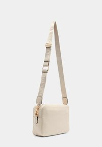 Rektangulær lædertaske i cremede farver med en struktureret finish, med en guldlynlås og et mønstret, justerbart rem til brug som crossbody.