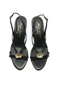 Sandalias negras tipo slingback con tiras estrechas, que presentan un acento dorado en el empeine y una textura mate suave. Diseño de punta cuadrada.