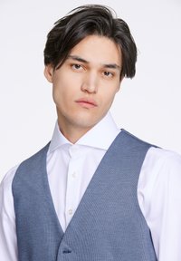 Ljusblå strukturerad väst över en vit skjorta, med en V-ringad design och subtila stuckaturer, samt en enkel knappstängning.