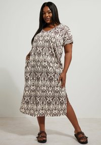 Maxi sukienka w kremowym kolorze z brązowym kwiatowym wzorem, krótki rękaw i boczne kieszenie. Zestawiona z czarnymi sandałami z ćwiekami.