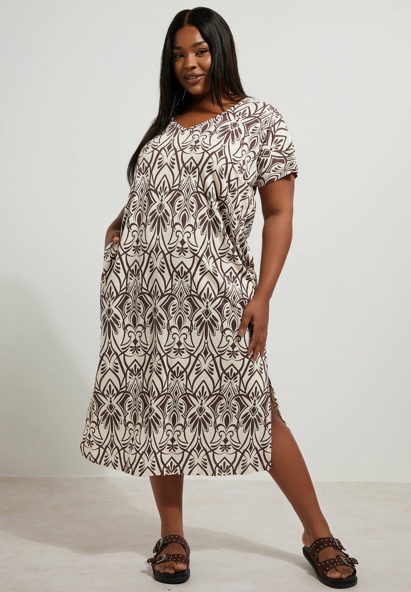 Maxi sukienka w kremowym kolorze z brązowym kwiatowym wzorem, krótki rękaw i boczne kieszenie. Zestawiona z czarnymi sandałami z ćwiekami.