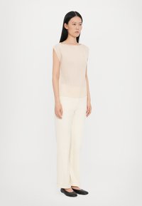 Beige ribbed knit top with cap sleeves, paired with cream wide-leg trousers and black flat shoes, creating a neutral palette.