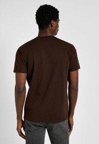 Camiseta de algodón marrón con cuello redondo y mangas cortas, que presenta una textura suave y un diseño simple y sin adornos.