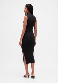 Schwarzes, geripptes Midikleid mit figurbetonter Silhouette, hohem Ausschnitt und seitlichem Schlitzdetail. Glatte Textur und ärmelloses Design.