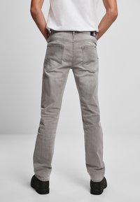 Jeans de denim gris vistos desde atrás. Cuenta con cinco bolsillos, ajuste de pierna recta y herrajes de color oscuro. Combinados con una camiseta blanca básica.