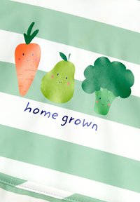Mönstrad tyg med gröna och vita ränder som har tecknade illustrationer av en morot, en päron och broccoli, med texten "hem odlad" nedan.
