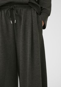 Pantalon en tissu doux gris foncé, avec une taille élastique et un cordon de serrage. Il dispose de poches latérales et d'un design décontracté à jambes larges.