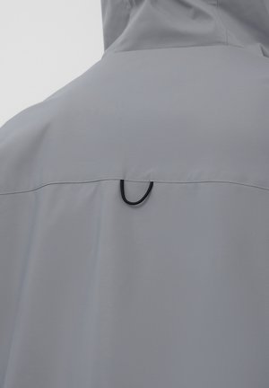 Vista posteriore di una giacca con cappuccio grigia che presenta una cucitura orizzontale con un piccolo anello nero nella parte superiore della schiena.