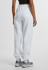 Witte sweatpants met een elastische tailleband en boorden, gemaakt van een zachte, fleece-achtige stof. Gecombineerd met grijze sportschoenen.
