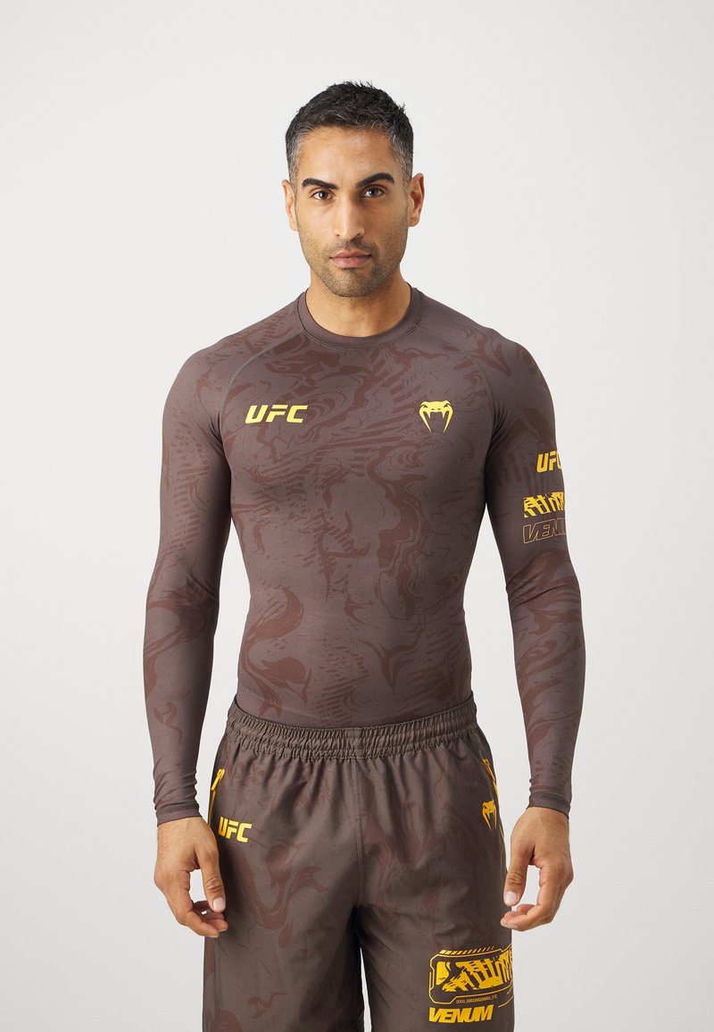 Langarmet, tettsittende rashguard i brun med subtilt mønster, med gule UFC- og Venum-logoer, sammen med matchende shorts.