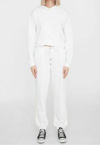 Vit croppad hoodie med huva och framficka, kombinerad med vita sweatpants med resår i midjan och svart dragsko.