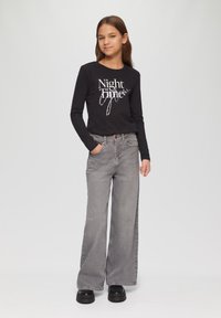 Zwarte longsleeve shirt met witte tekst "Night Time", gecombineerd met losse grijze jeans en dikke zwarte platform schoenen.