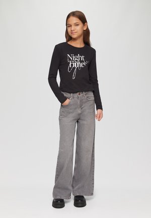 Zwarte longsleeve shirt met witte tekst "Night Time", gecombineerd met losse grijze jeans en dikke zwarte platform schoenen.