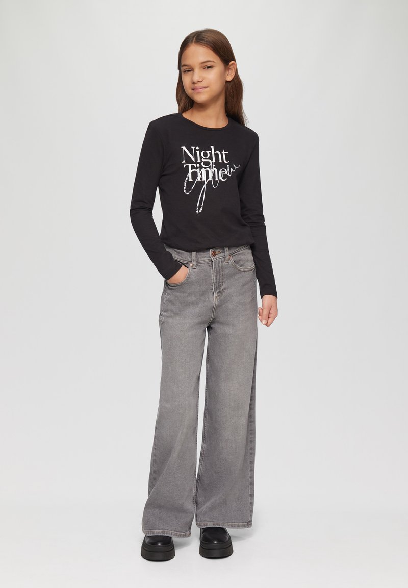 Zwarte longsleeve shirt met witte tekst "Night Time", gecombineerd met losse grijze jeans en dikke zwarte platform schoenen.
