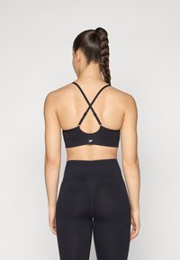 Sujetador deportivo negro con tirantes cruzados en la parte posterior, costuras planas y un branding mínimo. Combinado con leggings negros de cintura alta.