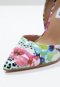 Chaussure à talons hauts à imprimé floral avec un bout pointu, présentant des couleurs vives comme le rose, le bleu et le vert, en matériau synthétique brillant.