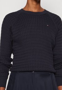 Dunkelblauer Strickpullover mit strukturiertem Muster, gerippten Bündchen und Rundhalsausschnitt. Kleines Logo-Detail auf der Brust.