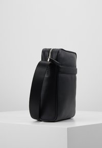 Borsa a tracolla in pelle nera con superficie texturizzata, forma rettangolare, chiusura con zip e tracolla regolabile. Design minimalista, senza hardware visibile.