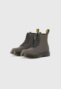 Botas cinzentas até ao tornozelo com um acabamento suave, sola de borracha, costuras amarelas e puxadores coordenados; apresentam atacadores e um fecho lateral.