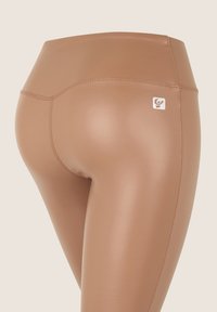 Leggings deportivos marrones con cintura alta, textura suave y un pequeño logo como detalle, con costuras planas para un ajuste aerodinámico.
