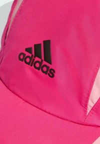 Růžová čepice Adidas z hladké látky s černým logem, vybavená zakřiveným kšiltem a panelovým designem, zdobená jemnými texturálními variacemi.