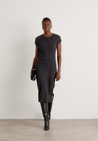 Black, fitted t-shirt dress with short sleeves, side slits, and a smooth texture, paired with knee-high black boots, and a clutch.