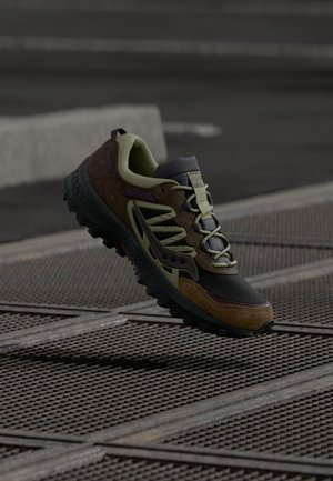 Vīriešu taku skriešanas apavi tumši zaļā un brūnā krāsā. Iespējama tekstūru melna gumijas zole, auklas un atbalstoša augšdaļa ar multicolor akcentiem.